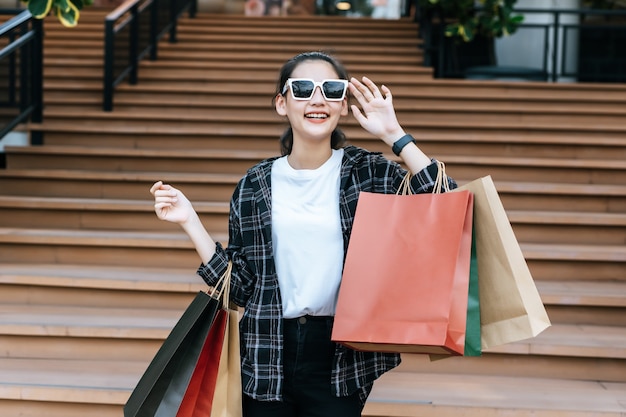 Portrait de jeune femme asiatique en masque facial portant des lunettes debout dans les escaliers avec un sac en papier commercial