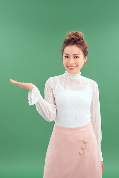 Portrait de jeune femme asiatique montrant sa main pour montrer le produit. Isolé sur fond vert.