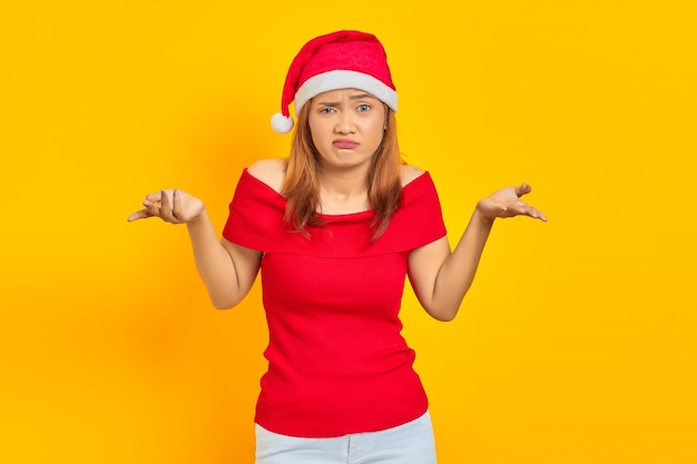 Portrait de jeune femme asiatique portant un chapeau de Noël ayant des doutes avec une expression faciale confuse