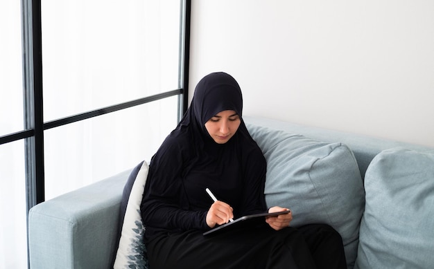 Portrait de jeune femme asiatique portant le hijab, travaillant à la maison avec iPad pro