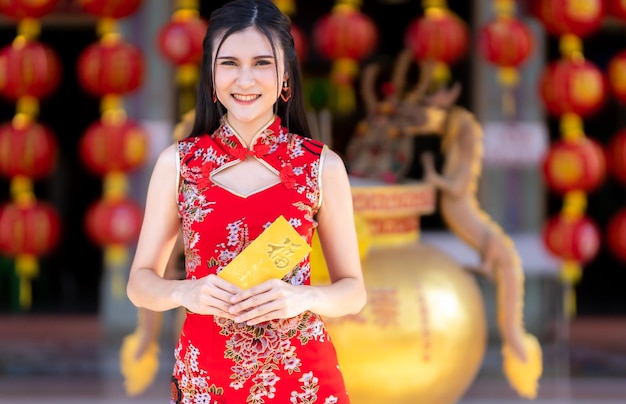 Portrait d'une jeune femme asiatique portant une robe rouge cheongsam décoration traditionnelle tenant des enveloppes jaunes avec le texte chinois Bénédictions écrites dessus est une bonne chance pour le festival du nouvel an chinois