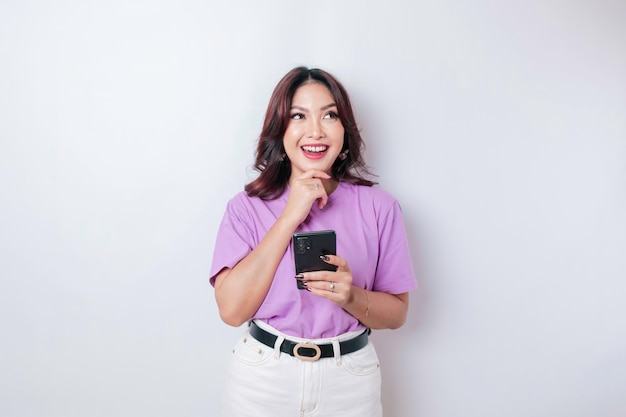 Portrait d'une jeune femme asiatique réfléchie portant un t-shirt violet lilas regardant de côté tout en tenant un smartphone