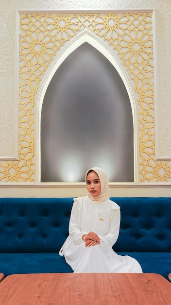 portrait d'une jeune femme asiatique souriante élégamment avec ses mains reposées sur ses genoux assise sur un s