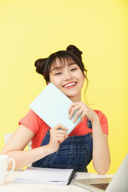 Portrait d'une jeune femme asiatique souriante avec un livre enthousiaste à l'idée de prendre un nouveau cours en ligne