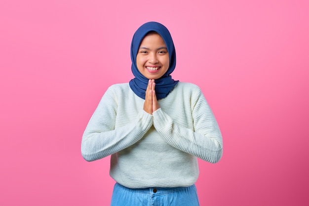 Portrait de jeune femme asiatique souriante montrant un geste de prière sur fond rose