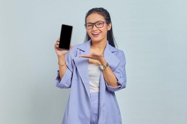 Portrait d'une jeune femme asiatique souriante pointant vers un téléphone à écran blanc avec paume isolé sur fond blanc