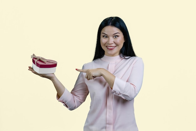 Portrait d'une jeune femme asiatique souriante pointe vers une boîte-cadeau en forme de coeur