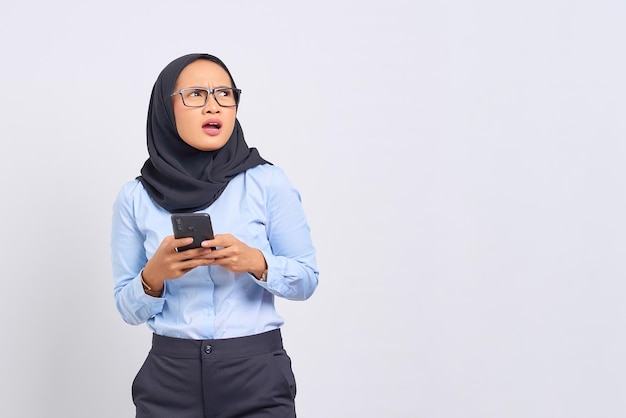 Portrait de jeune femme asiatique surprise à l'aide d'un téléphone mobile et à l'écart isolé sur fond blanc