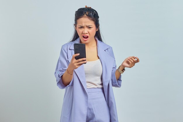 Portrait d'une jeune femme asiatique surprise avec la bouche ouverte et tenant un smartphone isolé sur fond blanc