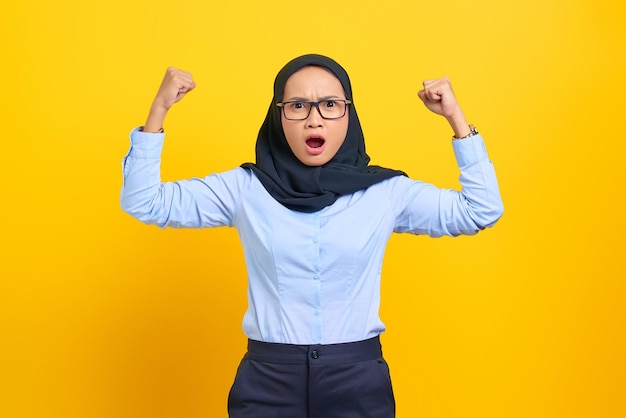 Portrait de jeune femme asiatique surprise lève les bras et montrant des biceps isolés sur fond jaune