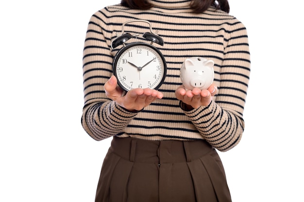 Portrait d'une jeune femme asiatique en uniforme décontracté tenant une tirelire blanche et un réveil isolés sur fond blanc Concept d'économie d'argent financier et bancaire