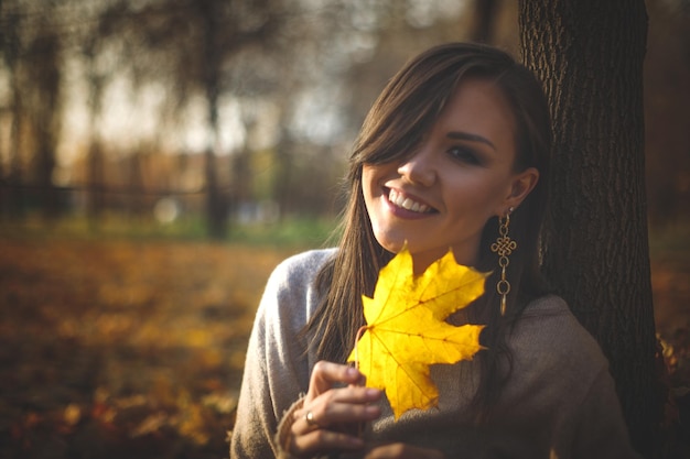 Photo portrait d'une jeune femme d'asie centrale avec une feuille d'érable jaune dans ses mains dans le parc d'automne du soir