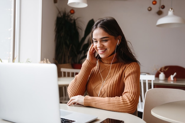 portrait d'une jeune femme assez belle assise dans un café à l'intérieur à l'aide d'un ordinateur portable.