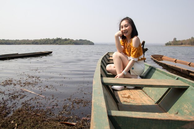 Portrait d'une jeune femme assise sur un bateau en mer contre un ciel clair