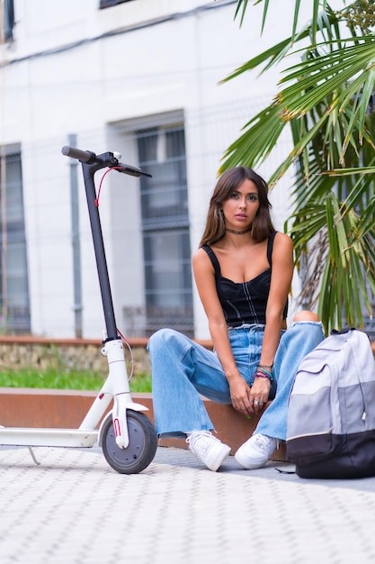 Portrait d'une jeune femme assise dans la ville attendant des amis avec un scooter électrique