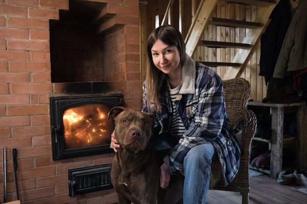 Photo portrait de jeune femme assise près de la cheminée avec son chien et regardant la caméra