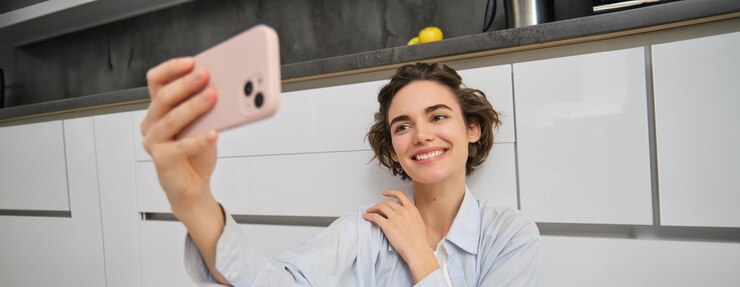 Portrait d'une jeune femme assise sur le sol de la cuisine avec un téléphone prenant un selfie sur un smartphone avec une application