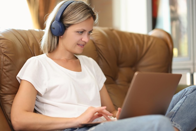 Portrait d'une jeune femme au casque assise sur un canapé et travaillant sur un ordinateur portable à distance de chat vidéo