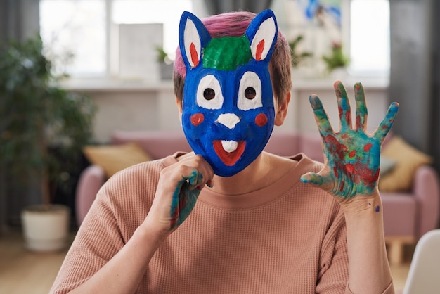 Portrait de jeune femme au masque de lapin peint assis à la maison