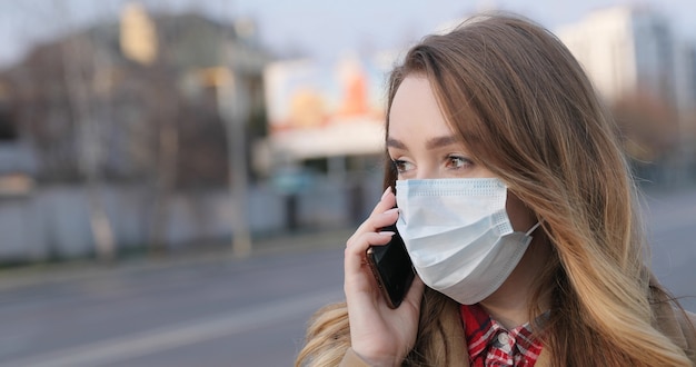 Portrait de jeune femme au masque médical parlant sur un smartphone dans la rue. Quarantaine de coronavirus. Concept de pandémie, épidémie de coronavirus.