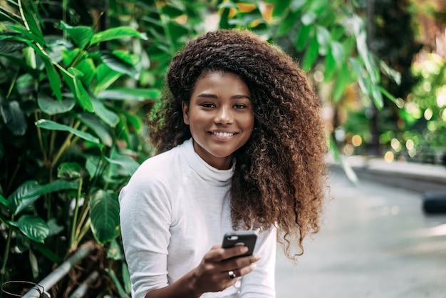 Portrait de jeune femme aux cheveux bouclés souriant tout en utilisant un téléphone portable.