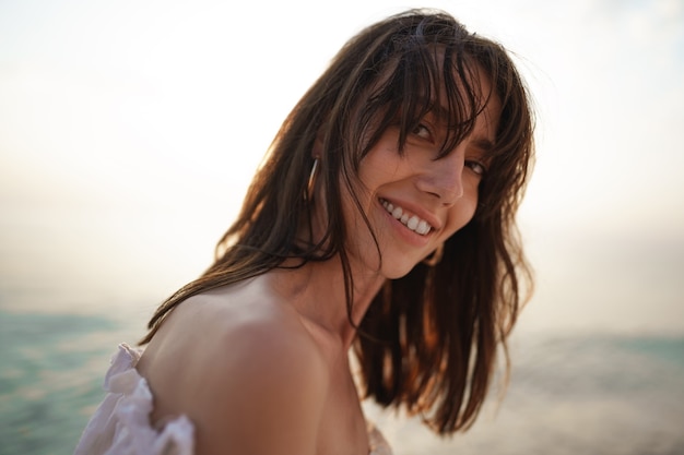 Portrait de jeune femme aux cheveux brune à la plage au coucher du soleil