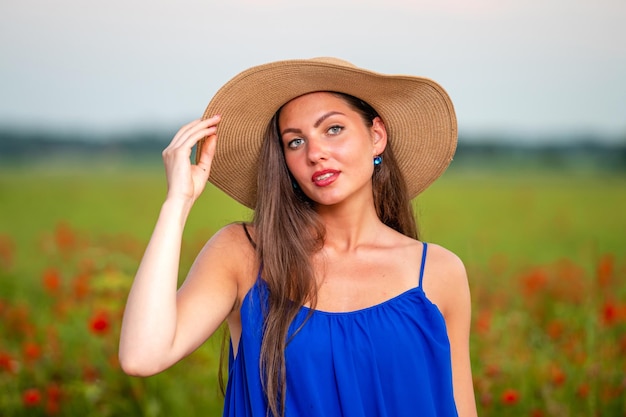 Portrait de jeune femme aux cheveux longs et chapeau de paille dans un champ de coquelicots au soleil du soir