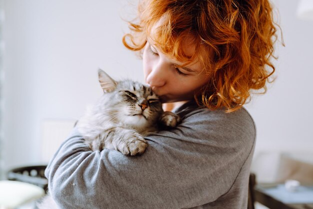 Portrait d'une jeune femme aux cheveux roux et bouclés avec un chat domestique moelleux et aimé