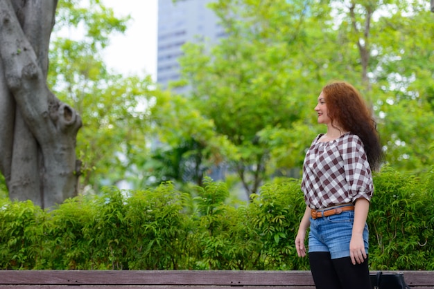 Portrait de jeune femme aux cheveux roux bouclés dans le parc en plein air