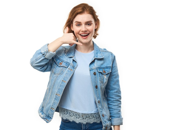 Portrait d'une jeune femme aux cheveux roux qui fait semblant d'appeler quelqu'un fait un signe d'appel avec des doigts isolés sur un fond blanc de studio donnez-moi un appel main en forme de téléphone