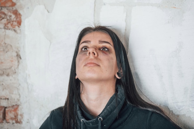 Portrait d'une jeune femme battue avec une ecchymose sous les yeux qui se tient debout et s'appuie sur le mur à l'intérieur dans un bâtiment abandonné