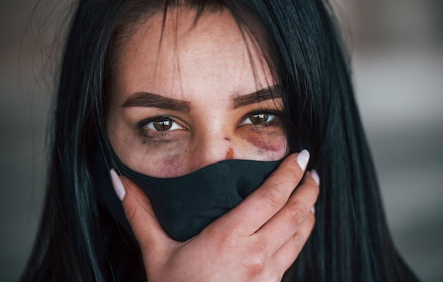 Portrait d'une jeune femme battue portant un masque de protection noir avec ecchymose sous les yeux à l'intérieur dans un bâtiment abandonné
