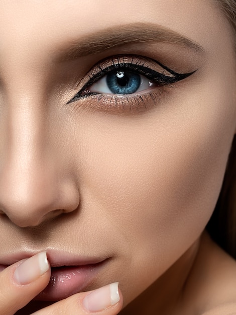 Portrait de jeune femme belle avec des ailes d'eyeliner de mode moderne touchant ses lèvres