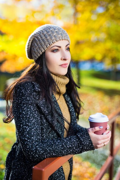 Portrait de jeune femme belle buvant du café dans le parc d'automne