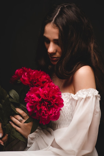 Portrait d'une jeune femme belle et sensuelle avec un luxuriant bouquet de pivoines rouges dans les mains