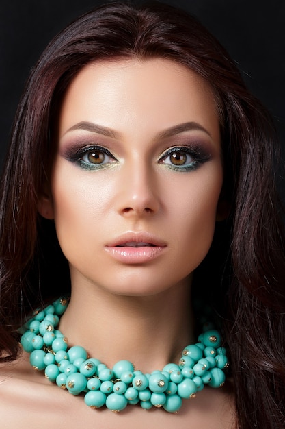 Portrait de jeune femme belle avec soirée maquillage portant collier bleu. Modèle posant sur fond sombre. Yeux charbonneux avec eye-liner. Concept de maquillage classique. Prise de vue en studio.