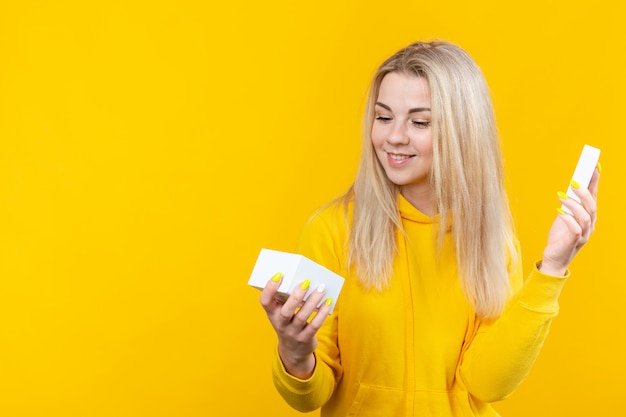 Portrait de jeune femme blonde assez caucasienne en costume sportif jaune, ouvrez une boîte cadeau blanche, isolée.
