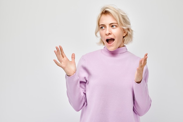 Portrait d'une jeune femme blonde au visage heureux souriant joyeusement avec les paumes levées et la bouche ouverte choquée isolée sur un fond de studio blanc