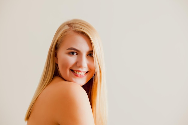 Portrait d'une jeune femme blonde avec un beau sourire regarde la caméra La femme à l'épaule nue est assise sur un fond beige