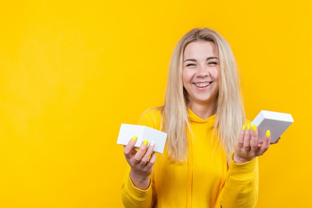 Portrait De Jeune Femme Blonde Caucasienne Joyeuse En Costume Sportif Jaune, Ouvrez Une Boîte Cadeau Blanche, Isolée.