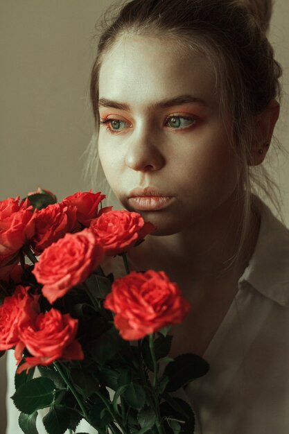 Portrait d'une jeune femme blonde avec du maquillage rouge et un bouquet de roses