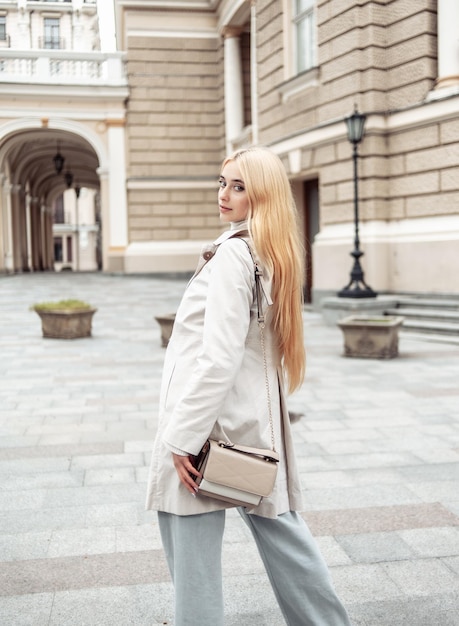 Photo portrait de jeune femme blonde fashion en trench-coat d'automne dans le contexte de l'architecture urbaine