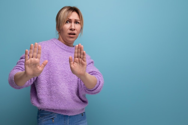 Portrait d'une jeune femme blonde indignée dans un pull lavande avec un signe de déni sur un fond lumineux