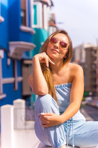 Portrait d'une jeune femme blonde séduisante portant des lunettes de soleil derrière une façade colorée bleue