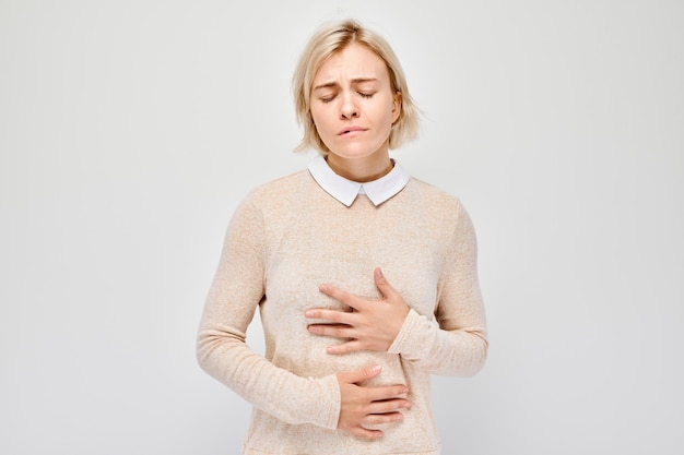 Portrait d'une jeune femme blonde souffrant de douleurs à l'estomac isolées sur fond blanc de studio Concept de problèmes intestinaux et gastriques