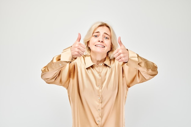 Portrait d'une jeune femme blonde en vêtements décontractés souriant joyeusement montrant le geste du pouce levé isolé sur fond blanc de studio approuve le bon choix bonne décision