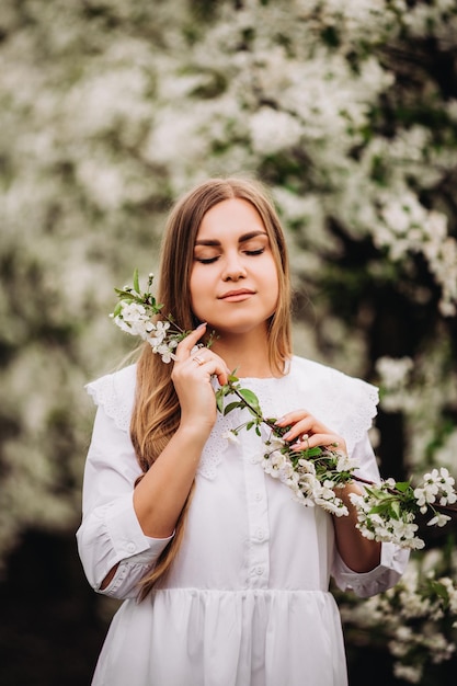 Le portrait d'une jeune femme blonde vêtue d'une robe blanche comme neige se tient près d'un pommier en fleurs. Une fille se promène dans un verger de pommiers en fleurs au printemps