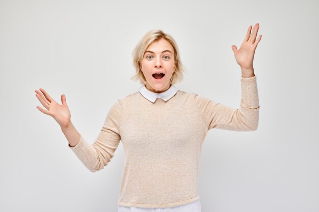 Portrait jeune femme blonde visage heureux souriant joyeusement avec les paumes surélevées et la bouche ouverte choquée isolée sur fond blanc de studio