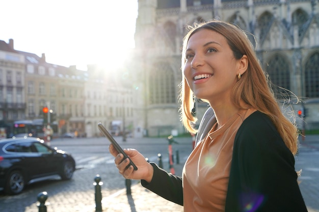 Portrait de jeune femme sur le bord de la route attendant un taxi tenant un téléphone intelligent Appeler un taxi avec un concept d'application téléphonique