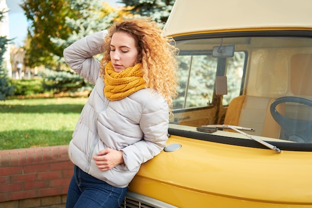 Portrait de jeune femme bouclée rousse attrayante restant devant la voiture jaune